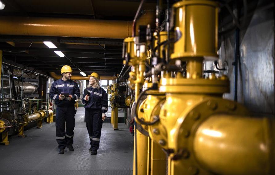 Two colleagues in PPE talking next to pipework